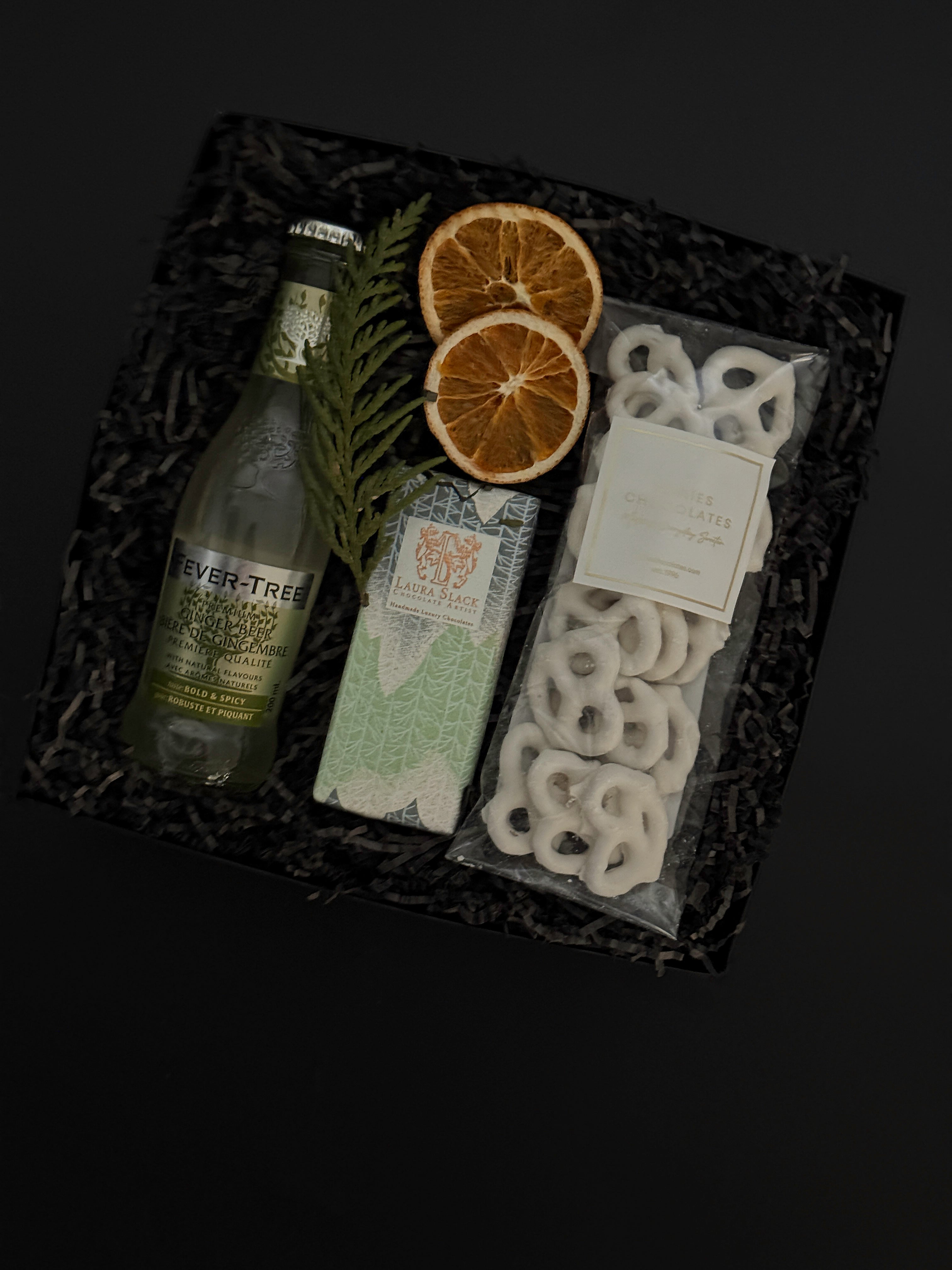 Holiday gift box with Fever-Tree ginger beer, chocolate, white chocolate pretzels and seasonal greenery