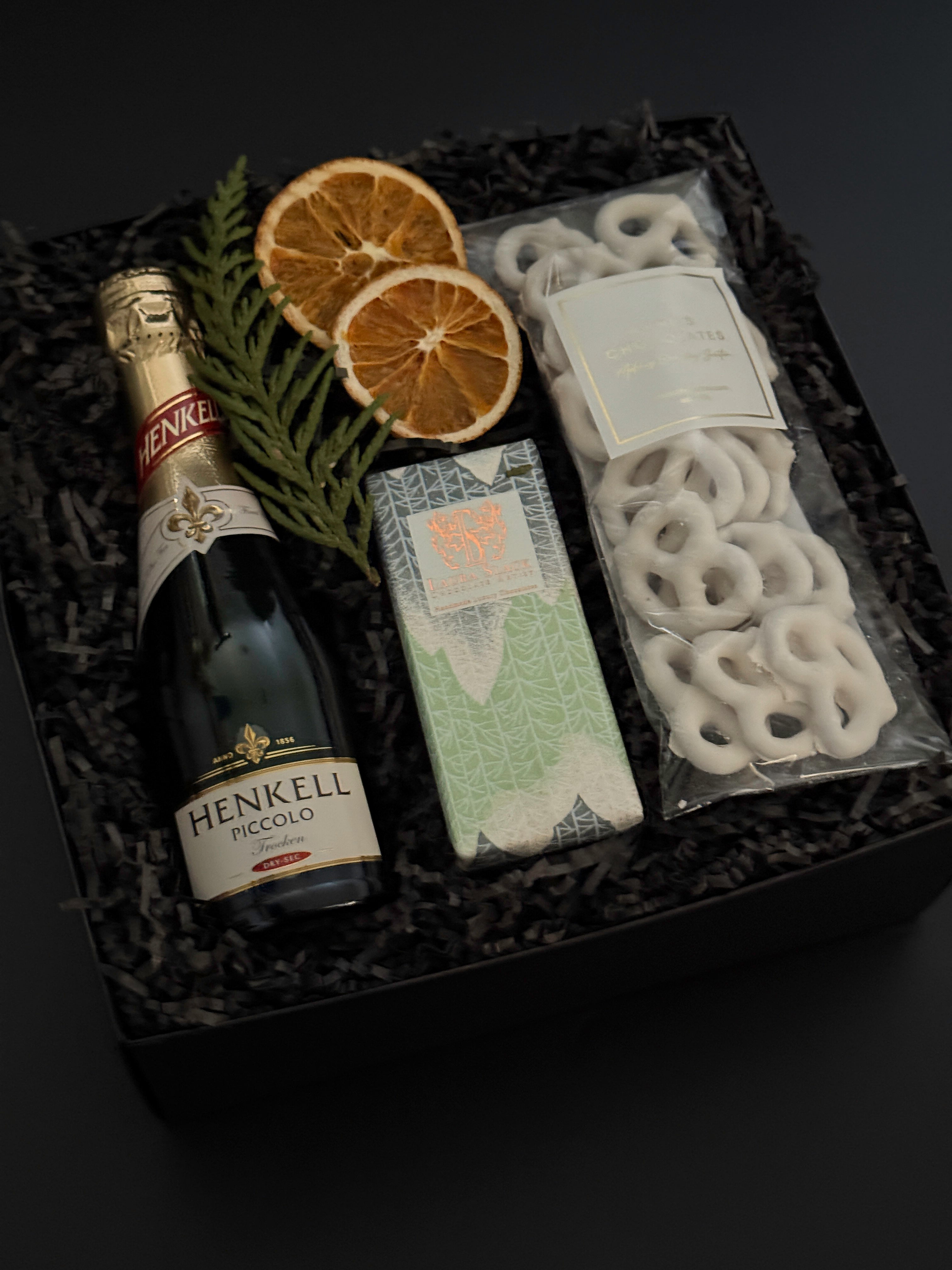 Corporate holiday gift box featuring Henkell sparkling wine, chocolate bar, and white chocolate pretzels.