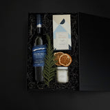 luxury black gift box with Cabernet Sauvignon, artisan chocolate, gold tin candle, and festive greenery, tied with grosgrain ribbon for a refined presentation.
