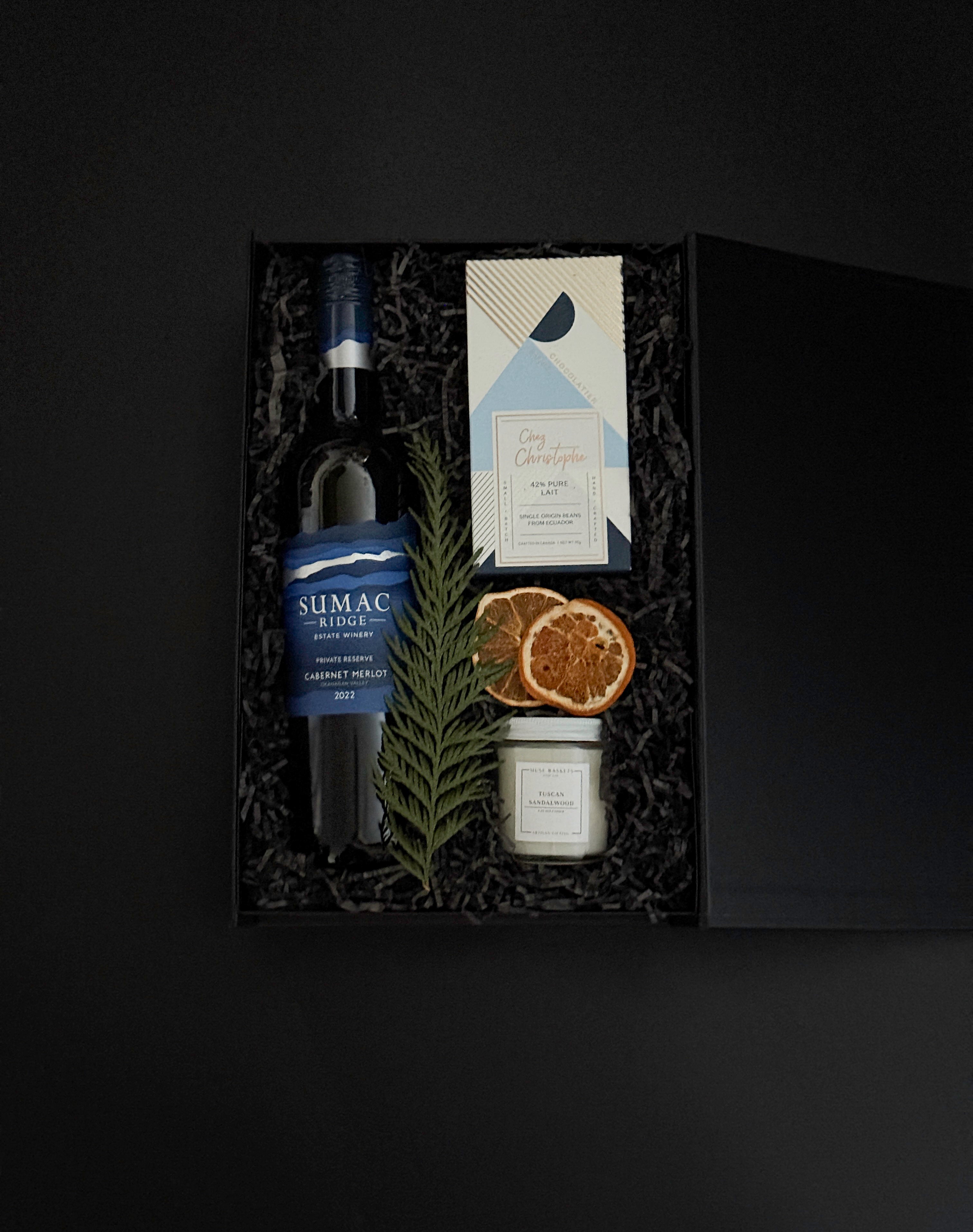 luxury black gift box with Cabernet Sauvignon, artisan chocolate, gold tin candle, and festive greenery, tied with grosgrain ribbon for a refined presentation.