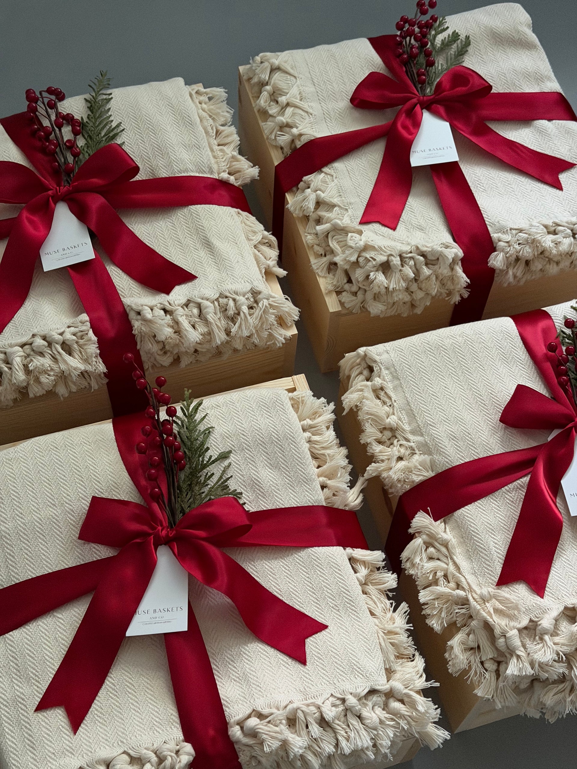 Gift boxes wrapped in white paper with red ribbons and greenery on a gray background