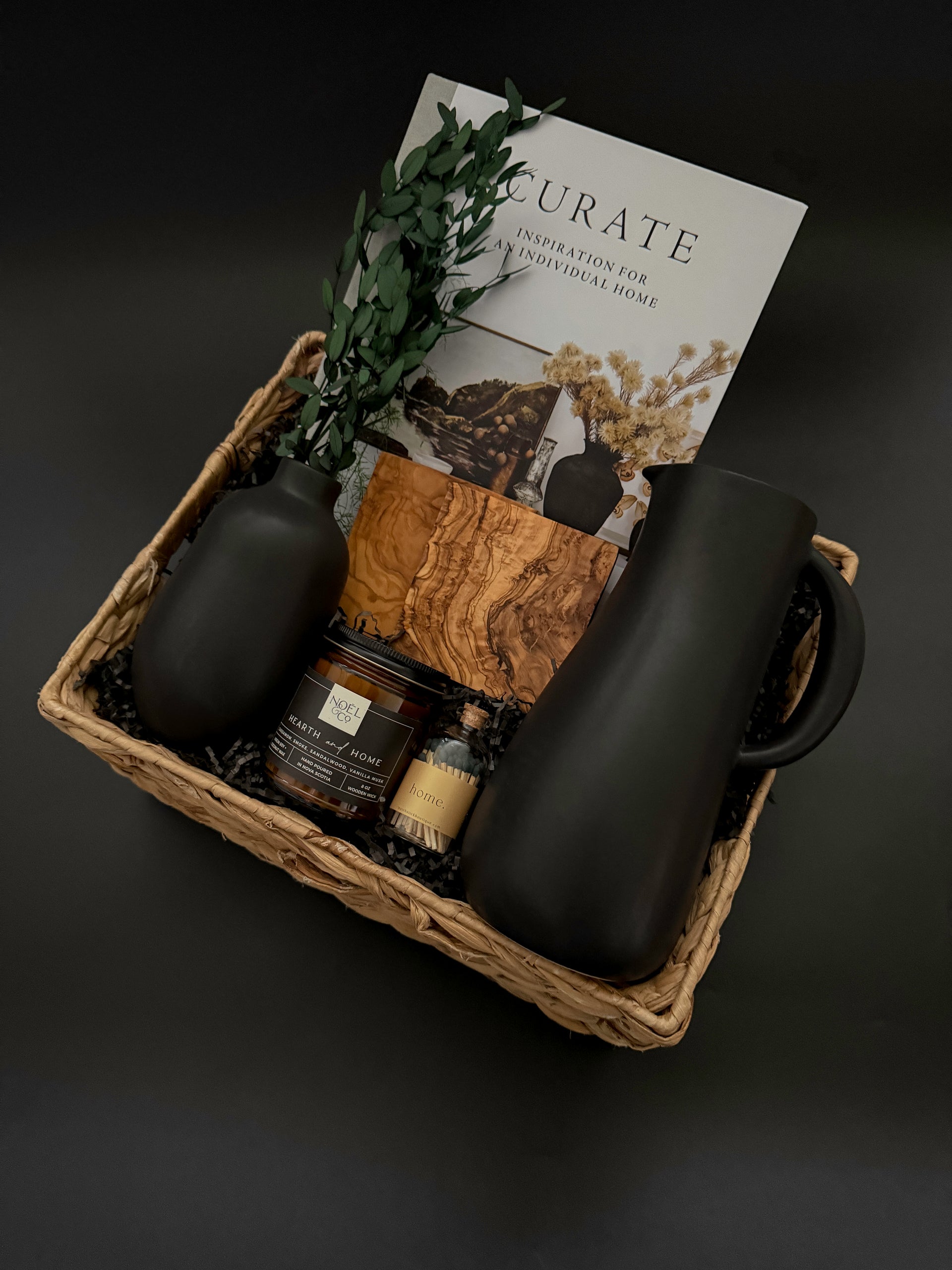 Gift basket with black mug, candle, and decorative item on a dark background