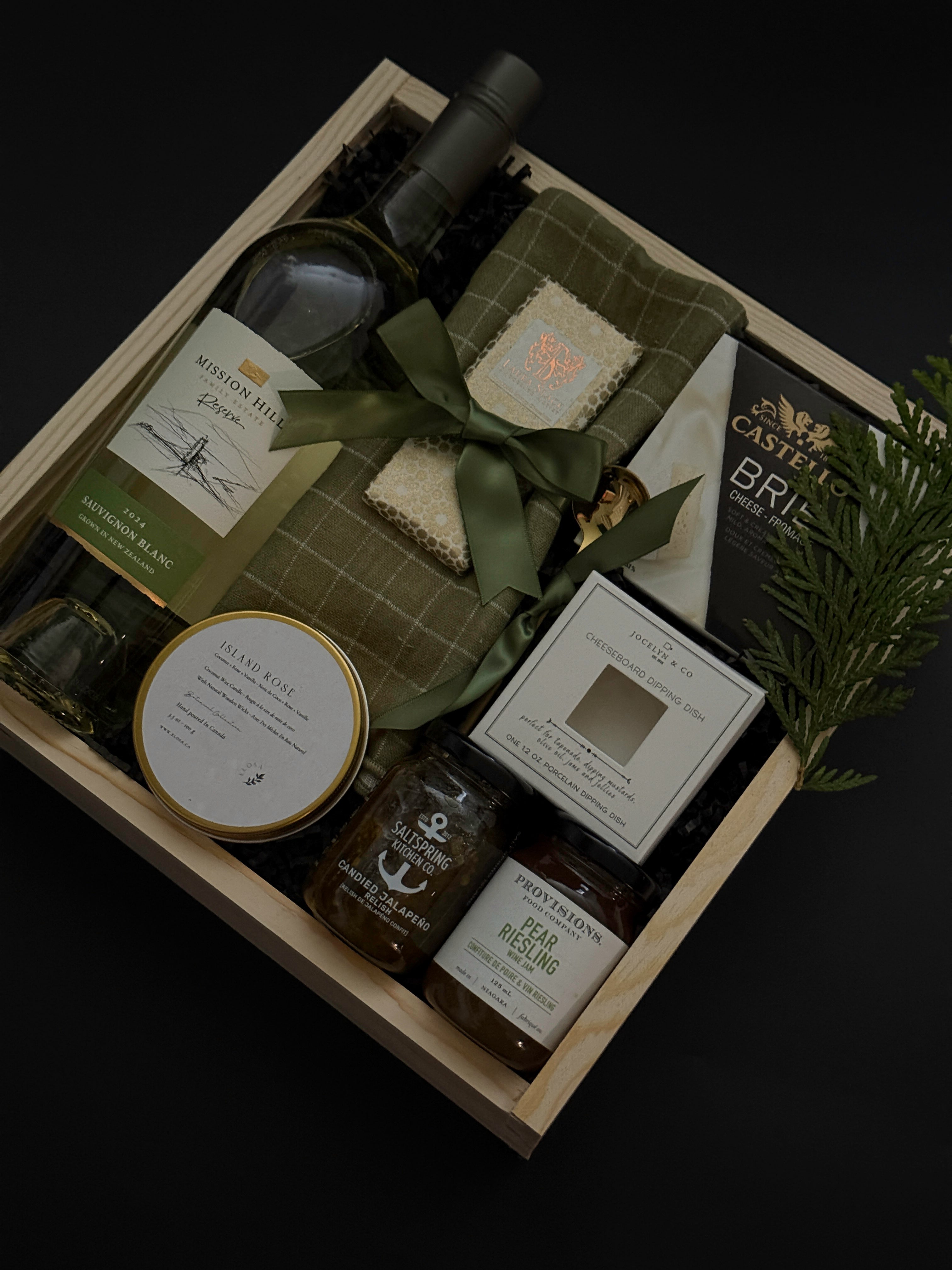 Charcuterie-inspired holiday gift box with wine, cheese, preserves, chocolate, and festive greenery — an elevated gift for corporate clients and office teams.