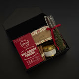 Gift set with white chocolate cranberry cookies, a candle, and other items in a black box on a dark background.