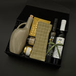 Gourmet food gift box with balsamic vinegar, olive oil, almonds, honey, and plaid tea towel.