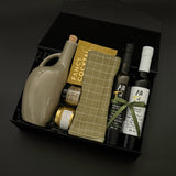 Gourmet food gift box with balsamic vinegar, olive oil, almonds, honey, and plaid tea towel.