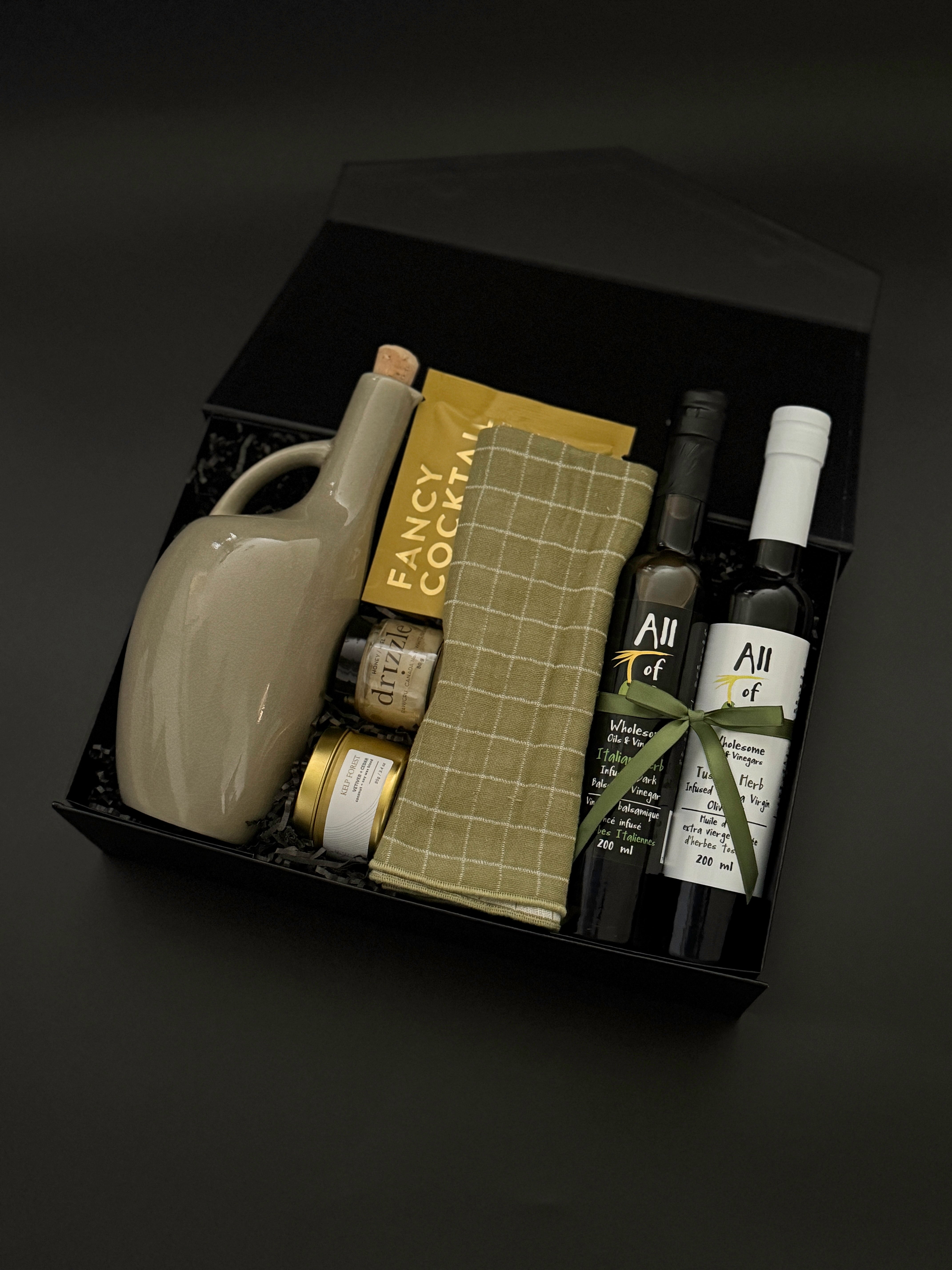 Gourmet food gift box with balsamic vinegar, olive oil, almonds, honey, and plaid tea towel.