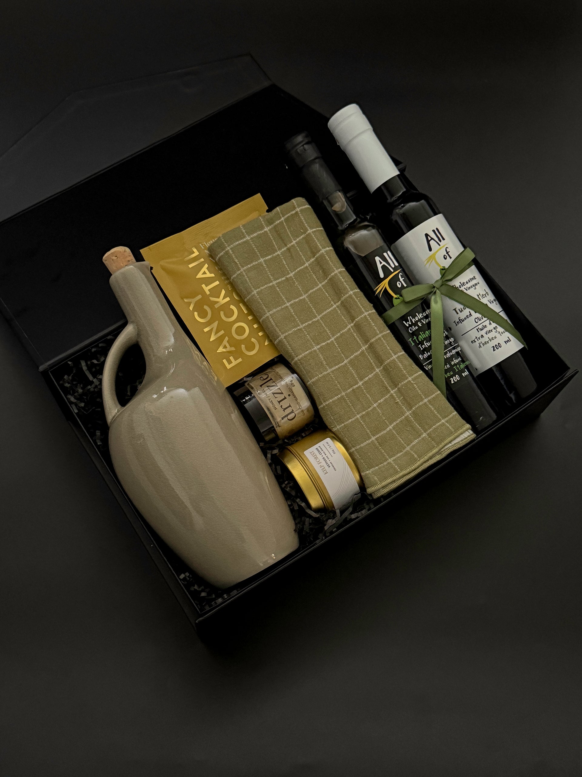 Gift set with ceramic jug, olive oil, and other items on a dark background