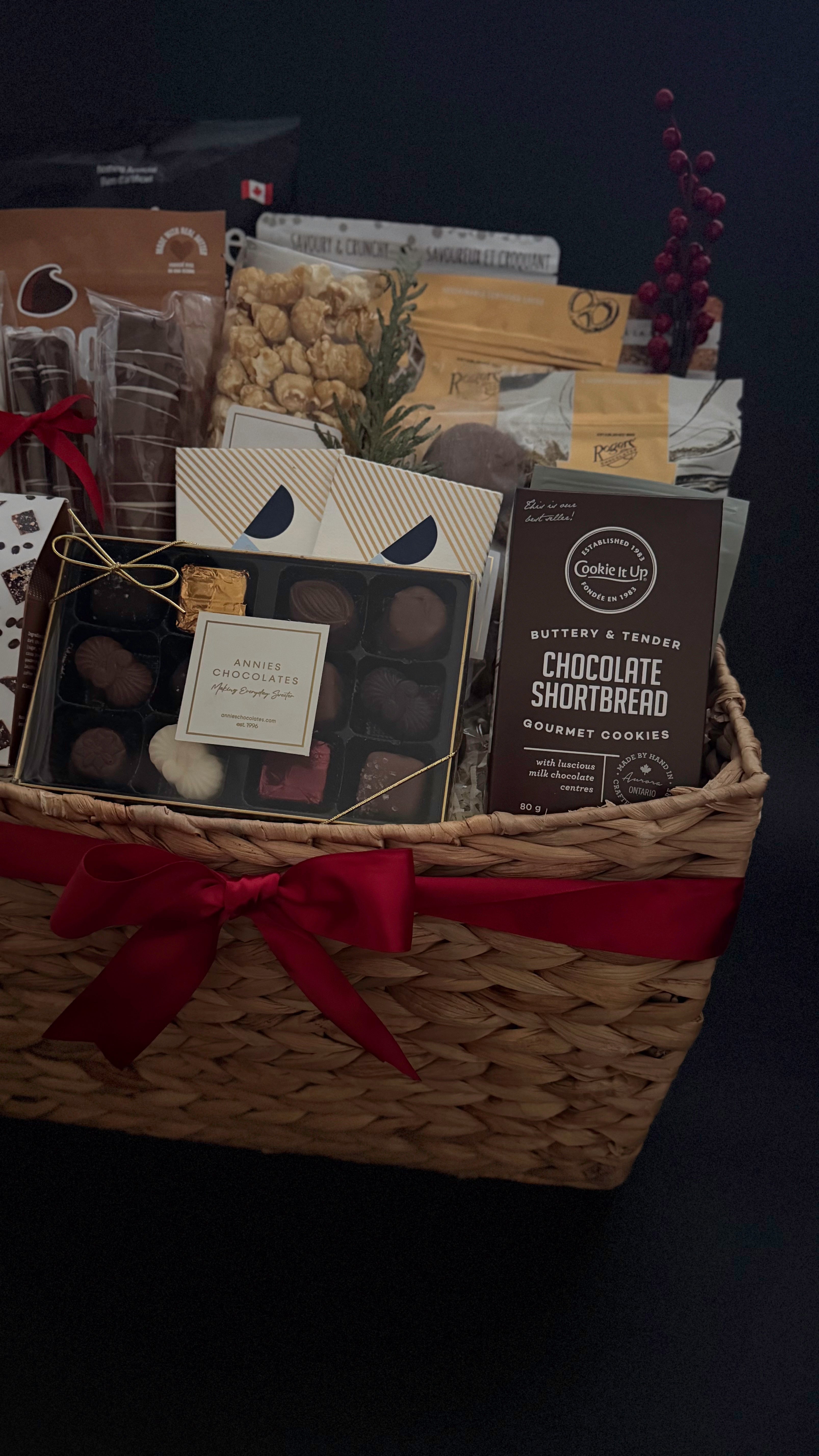 Gift basket with assorted items including a box of chocolates and a bag of cookies on a dark background.
