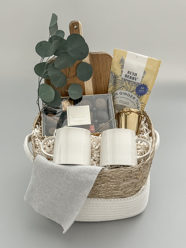 Luxury tea and chocolate gift basket with gold tea steeper, stoneware mugs, and Canadian artisanal treats, presented in a woven basket with satin ribbon