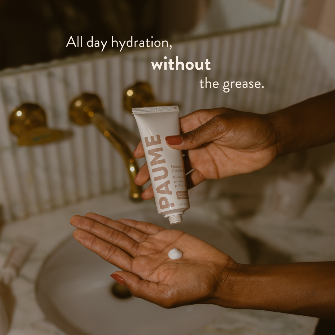 Hand holding a tube of Paume skincare product with text about hydration in a bathroom setting.