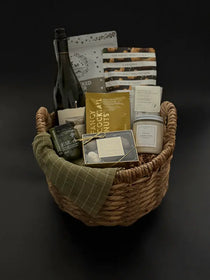 Grounded luxury gift basket with wine, candle, truffles, and savoury snacks in wicker basket