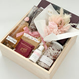 Gift box with bath products, a small bouquet, and boxed chocolates in wood basket and on a white background