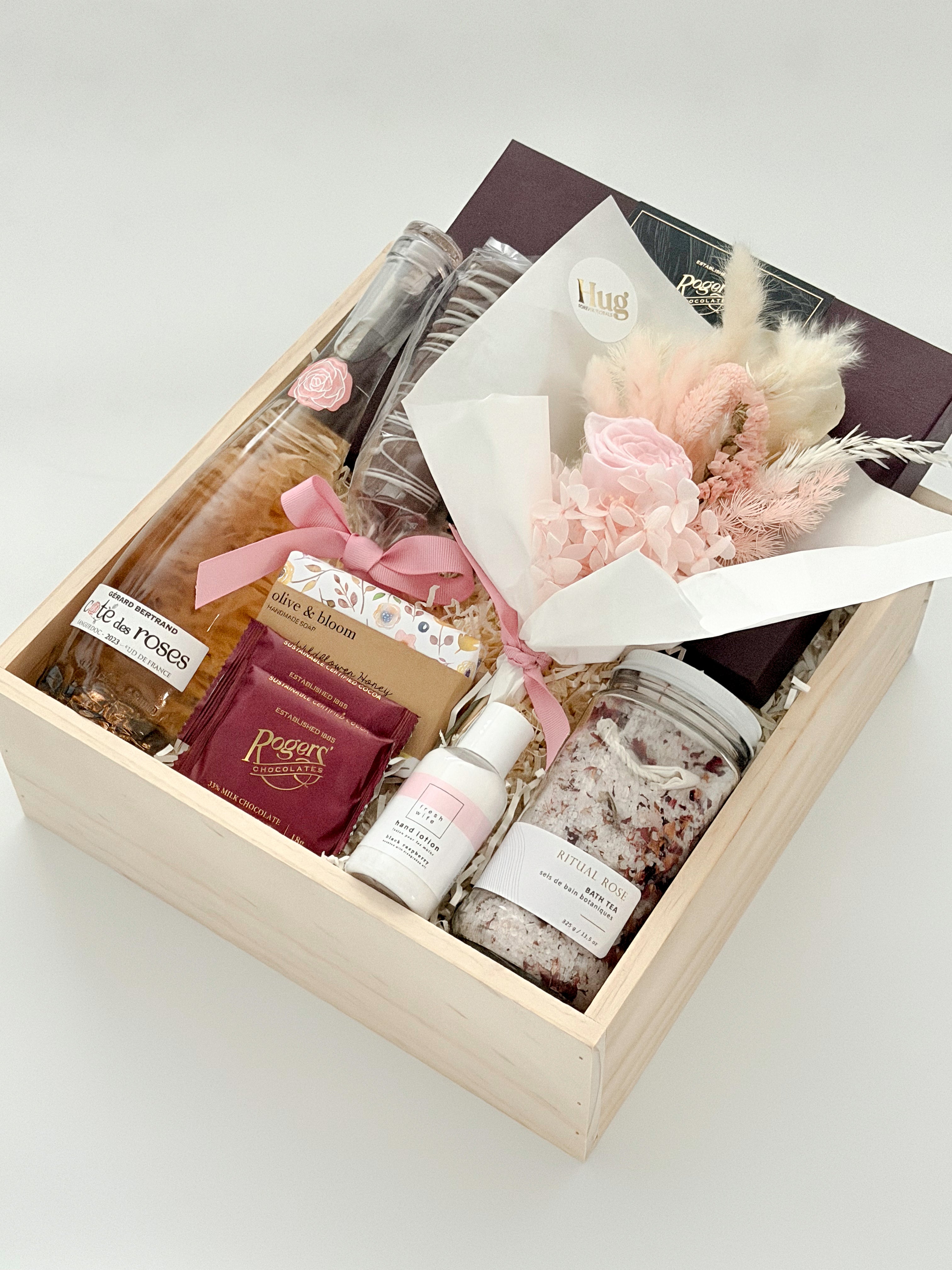 Gift box with bath products, a small bouquet, and boxed chocolates in wood basket and on a white background