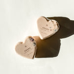 Two heart-shaped Adore bath bombs with dried floral accents, a self-care product featured in Muse Baskets and Co. gift baskets