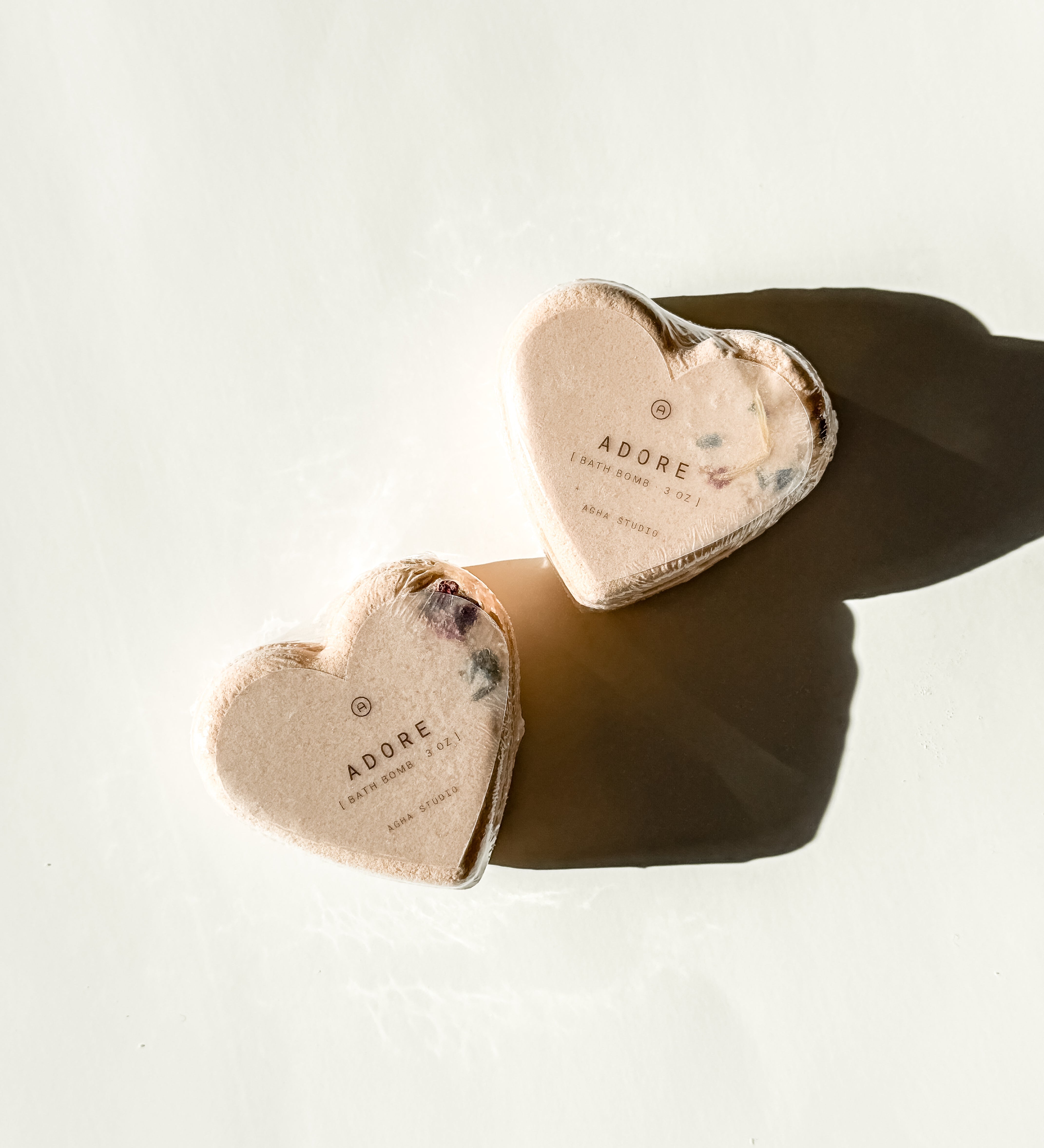 Two heart-shaped Adore bath bombs with dried floral accents, a self-care product featured in Muse Baskets and Co. gift baskets