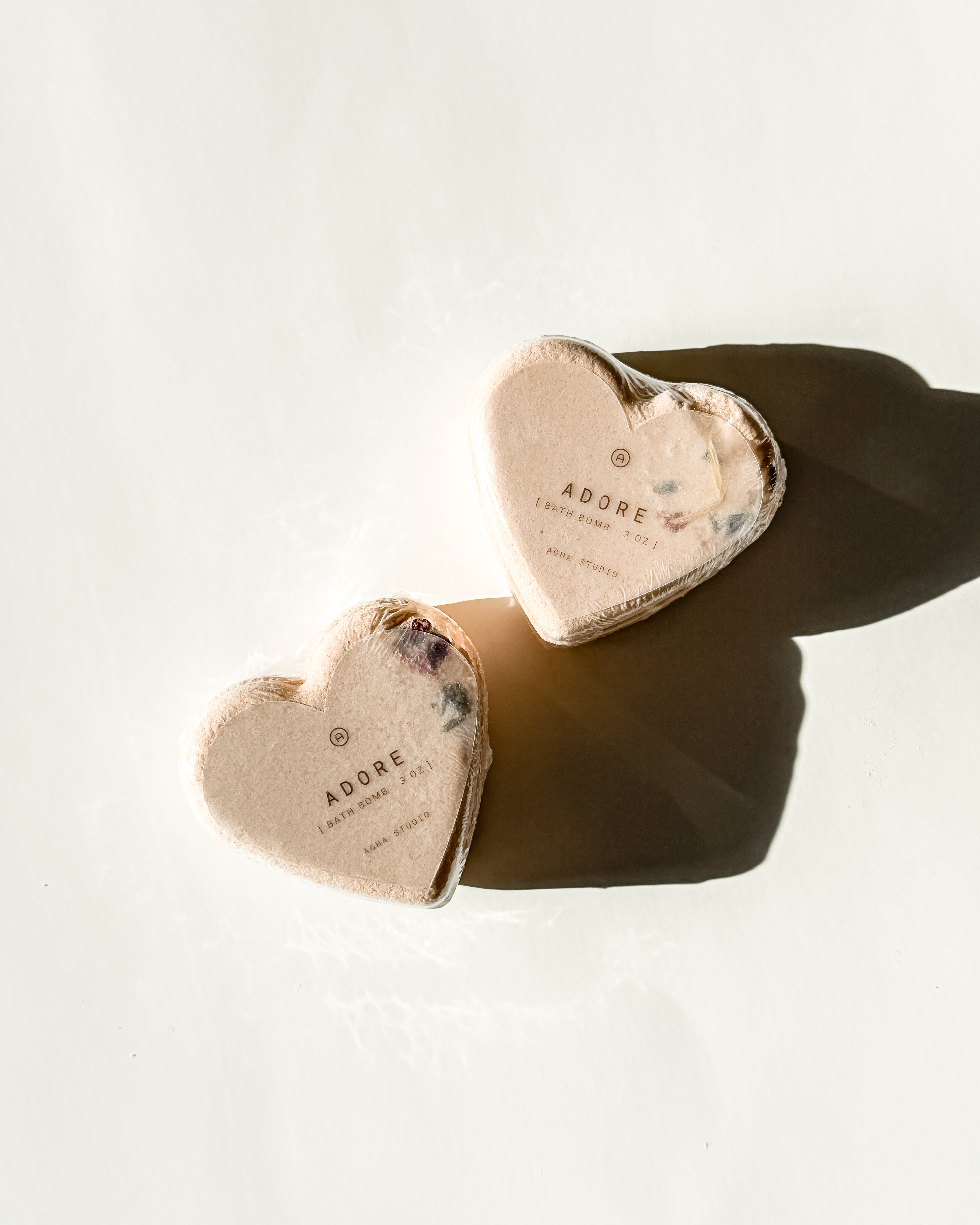 Two heart-shaped Adore bath bombs with dried floral accents, a self-care product featured in Muse Baskets and Co. gift baskets