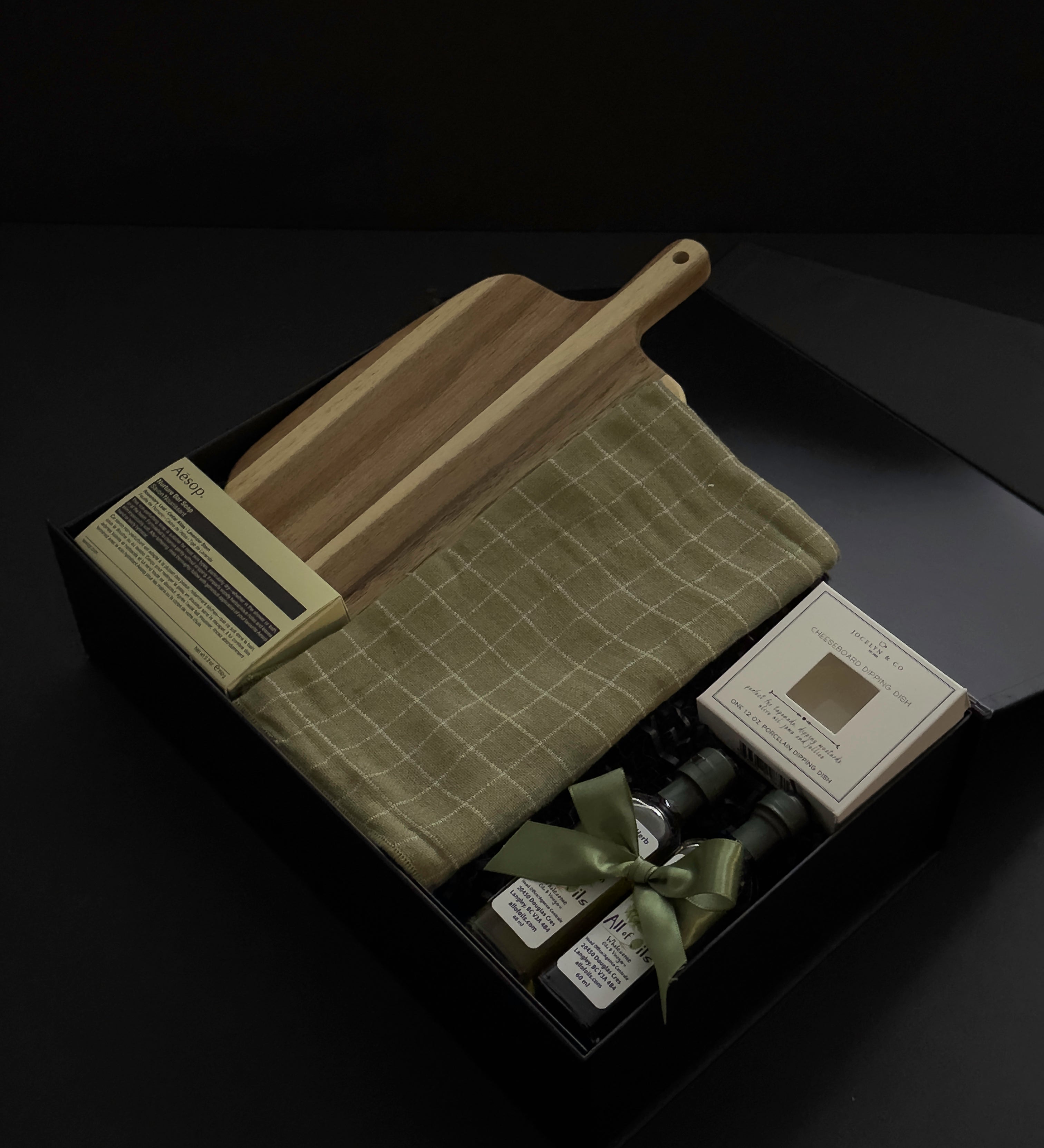 Open black Hestia realtor closing gift box with Aēsop soap, acacia wood board, green plaid tea towel, olive oil and balsamic vinegar by Muse Baskets and Co.