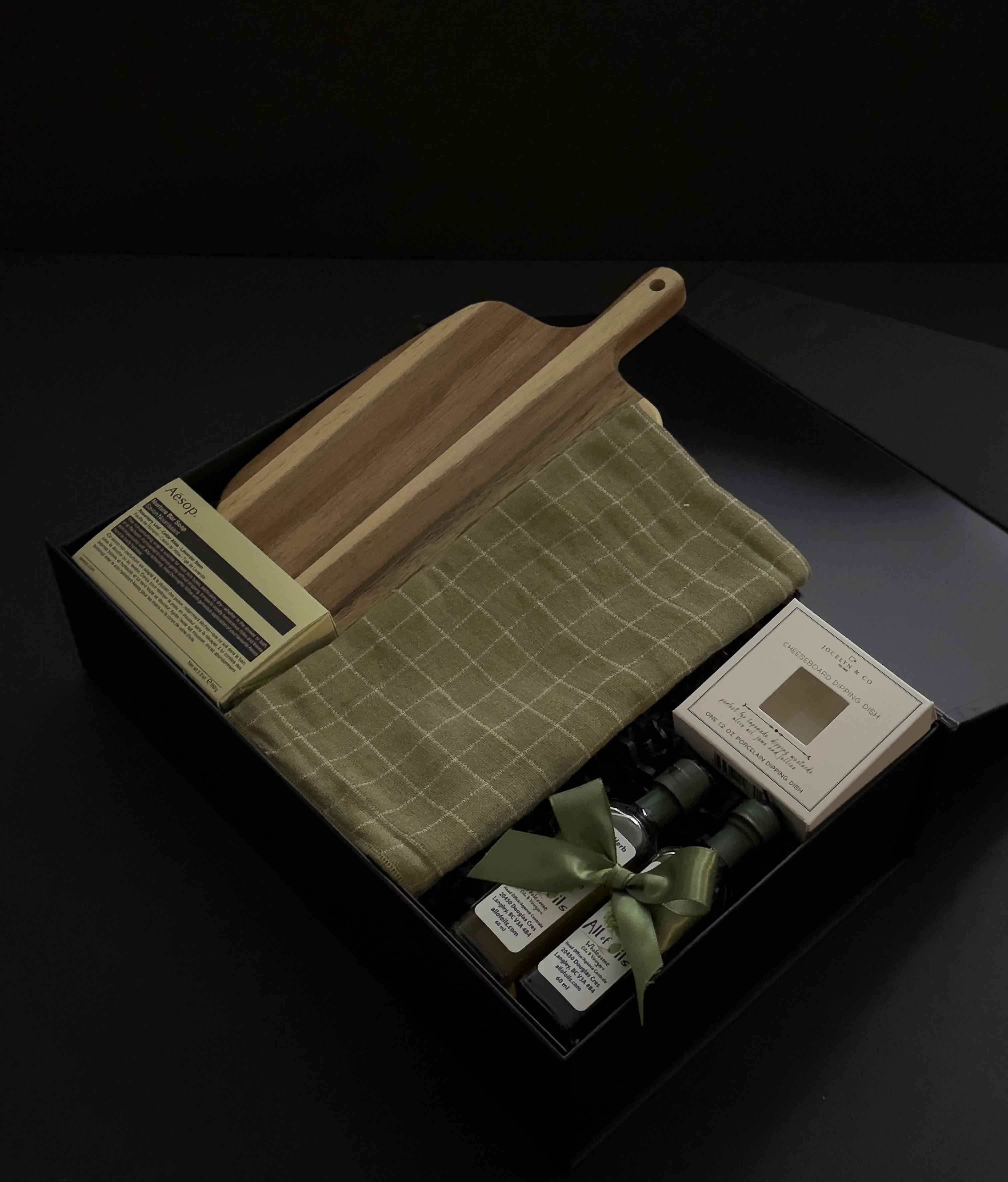 Open black Hestia realtor closing gift box with Aēsop soap, acacia wood board, green plaid tea towel, olive oil and balsamic vinegar by Muse Baskets and Co.