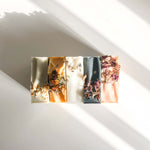 Row of Agha Studio soap bars with dried floral inclusions in varied colors, a self-care product featured in Muse Baskets and Co. gift baskets