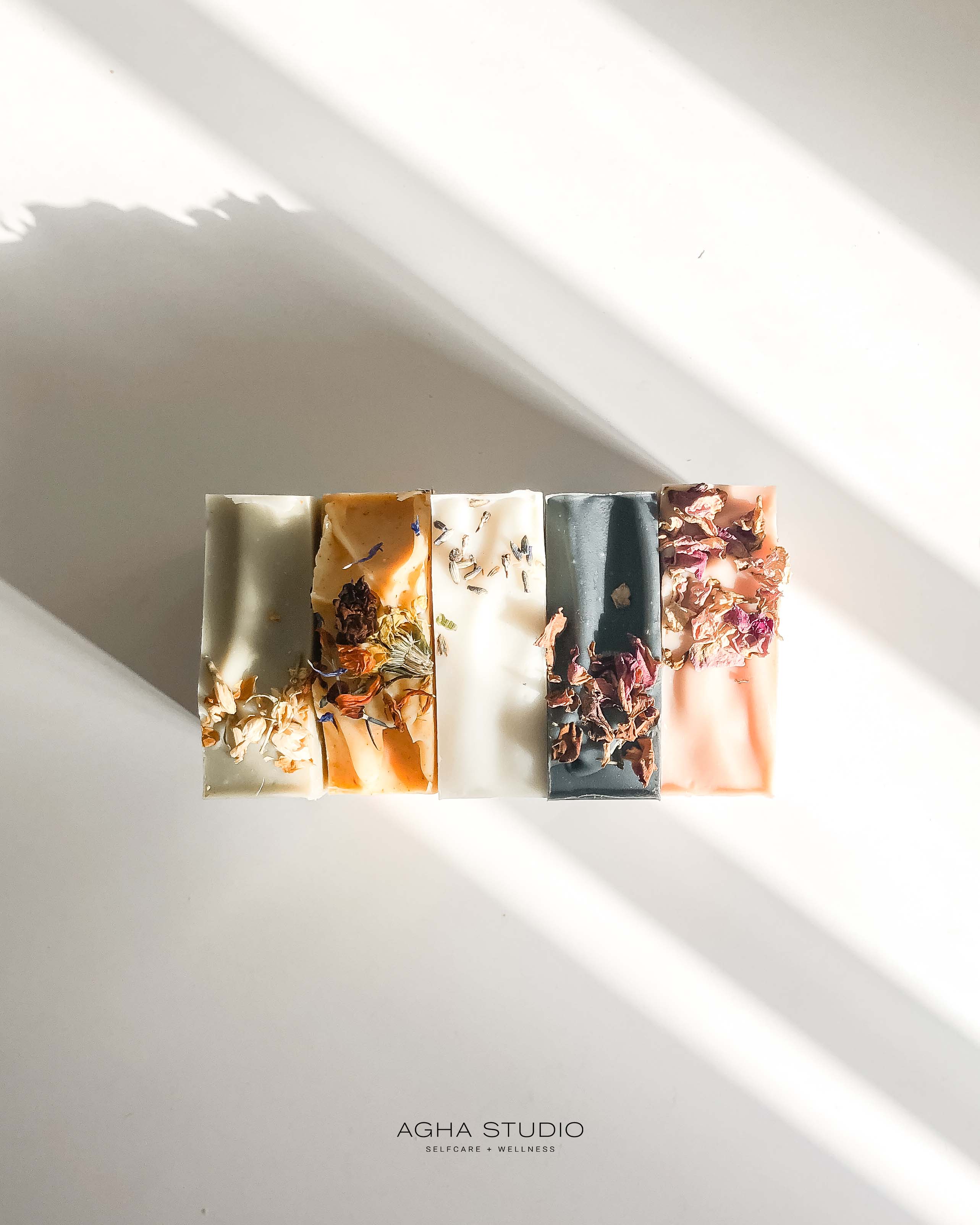 Row of Agha Studio soap bars with dried floral inclusions in varied colors, a self-care product featured in Muse Baskets and Co. gift baskets