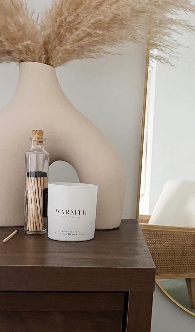 Candle labeled 'Warmth' on a wooden surface with decorative elements.