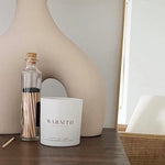 Candle labeled 'Warmth' on a wooden surface with decorative elements.