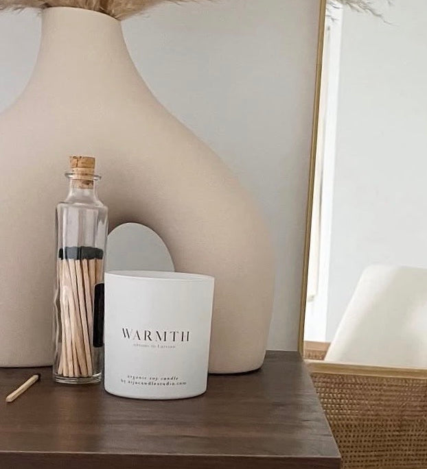 Candle labeled 'Warmth' on a wooden surface with decorative elements.