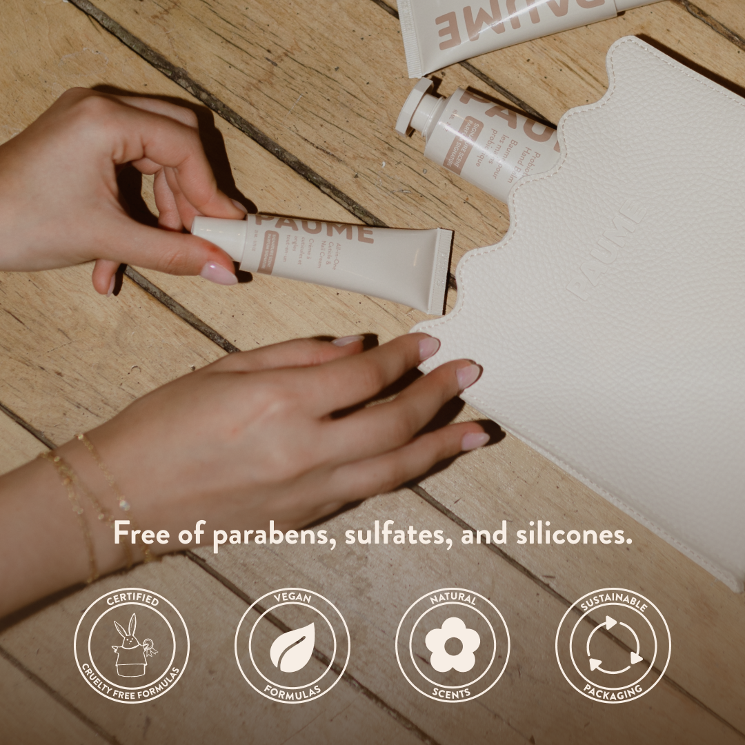 Hand holding a tube of cream on a wooden floor with product packaging in the background, featuring text about product ingredients and certification logos.
