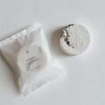 Aqua Studio Hinoki shower steamer beside its packaging pouch, a self-care product featured in Muse Baskets and Co. gift baskets
