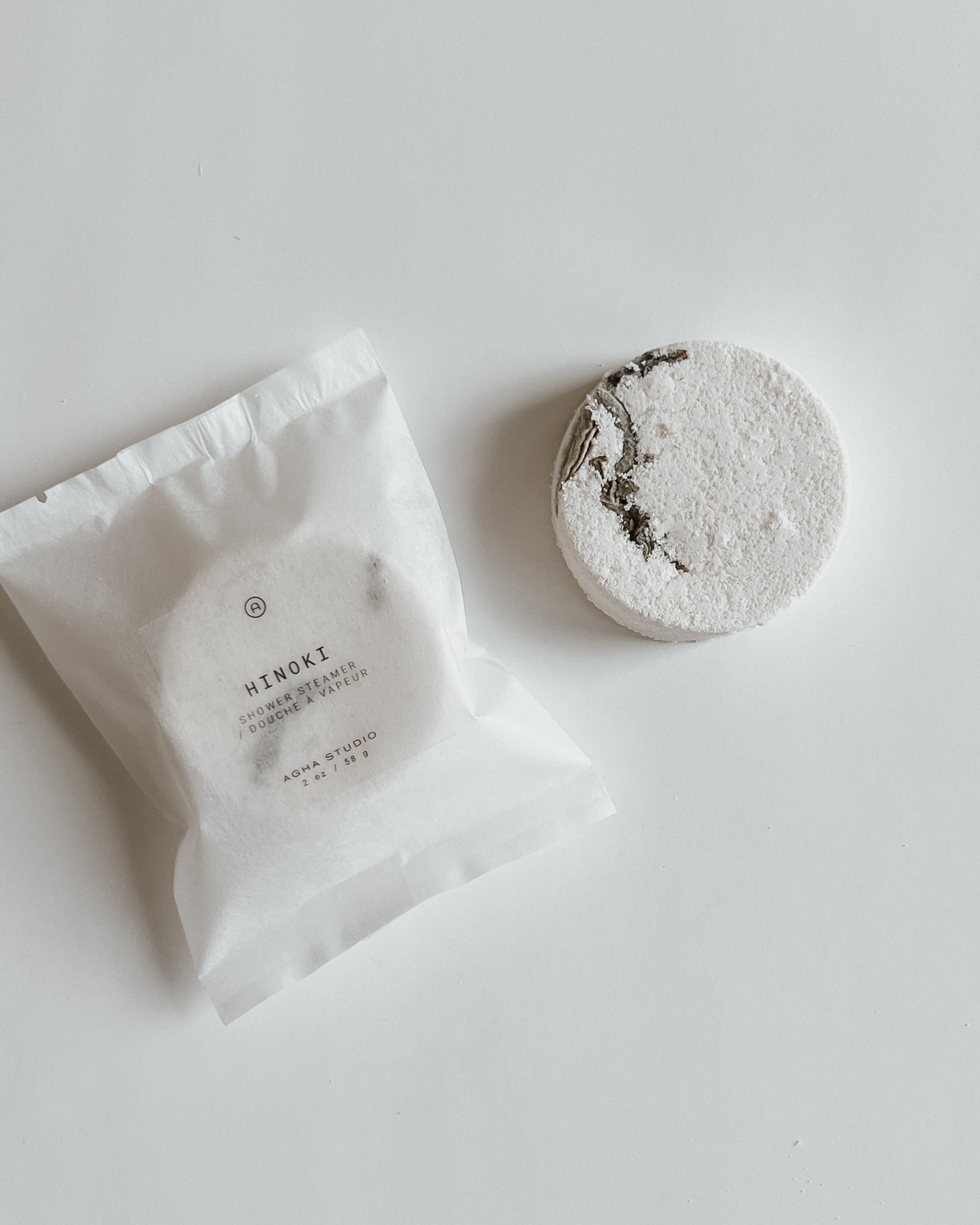 Aqua Studio Hinoki shower steamer beside its packaging pouch, a self-care product featured in Muse Baskets and Co. gift baskets