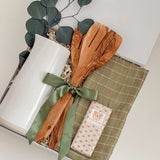 Decorative set with a white candle, wooden spoon, green ribbon, and a checkered cloth on a white surface.