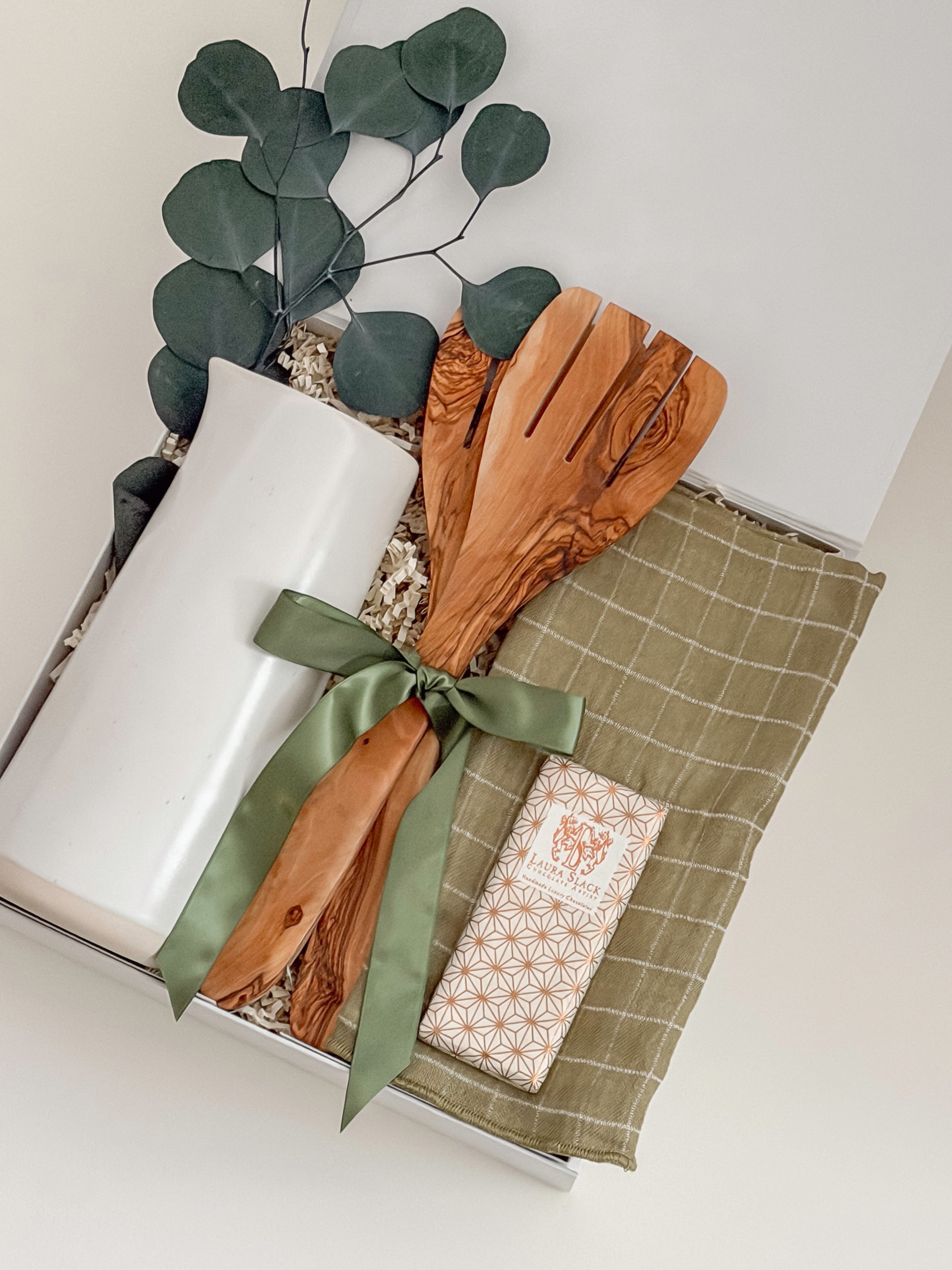 Decorative set with a white candle, wooden spoon, green ribbon, and a checkered cloth on a white surface.