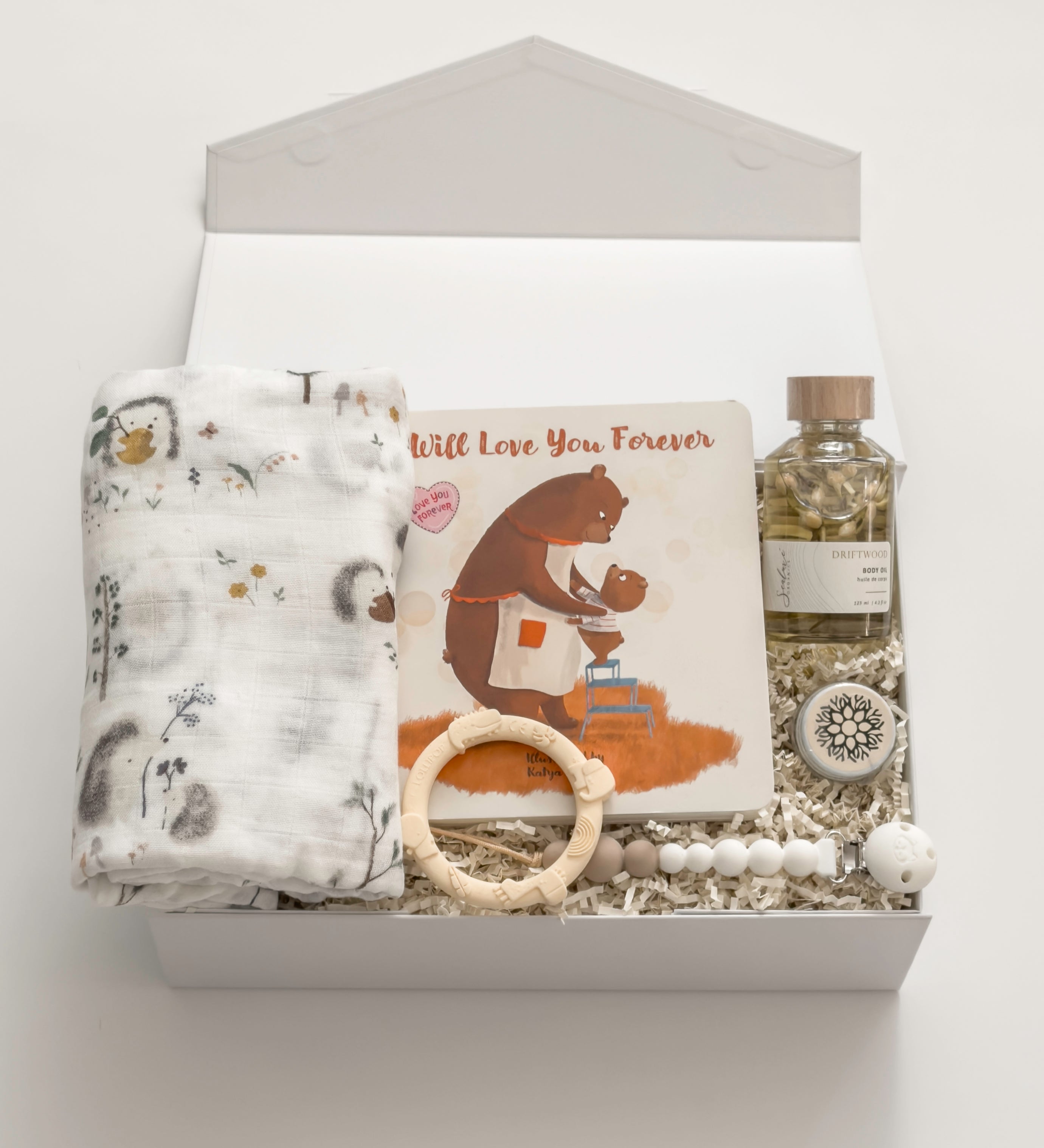 The Arrival gender-neutral new baby gift box by Muse Baskets and Co. with hedgehog swaddle, storybook, teething ring, pacifier clip and care products for mama.