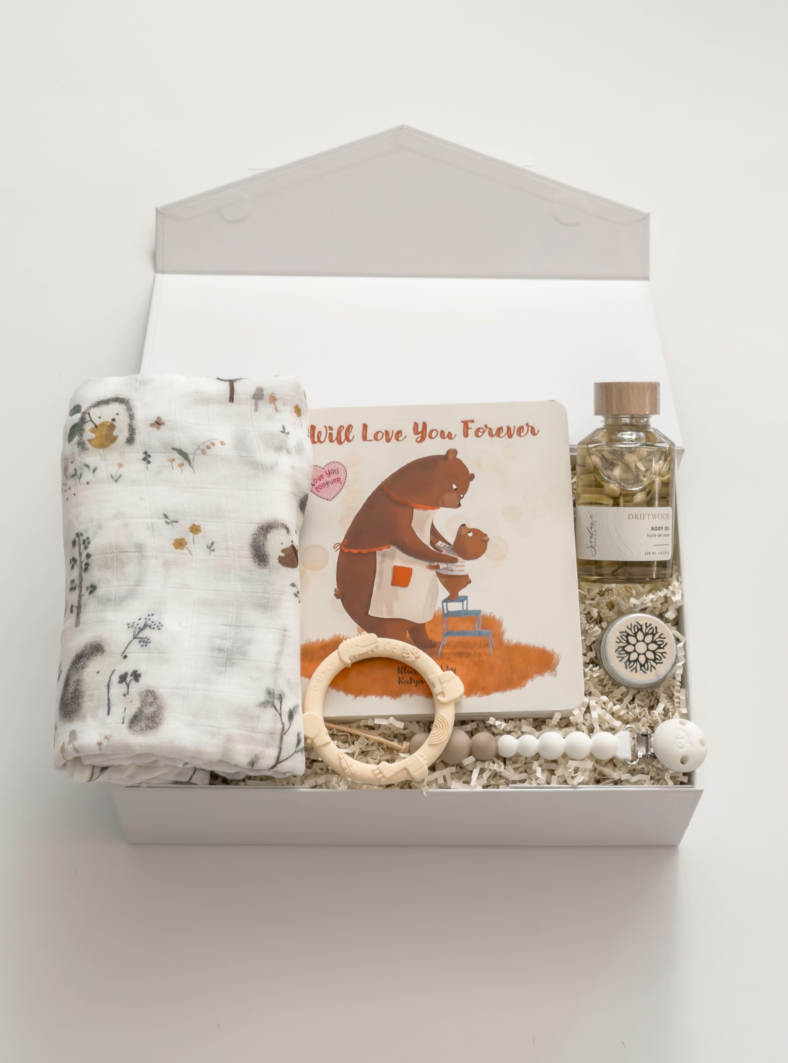 The Arrival gender-neutral new baby gift box by Muse Baskets and Co. with hedgehog swaddle, storybook, teething ring, pacifier clip and care products for mama.