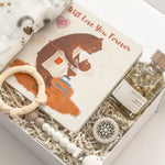 Gender-neutral baby gift for new parents by Muse Baskets and Co., presented in a signature white gift box with a swaddle, keepsake book and newborn essentials.