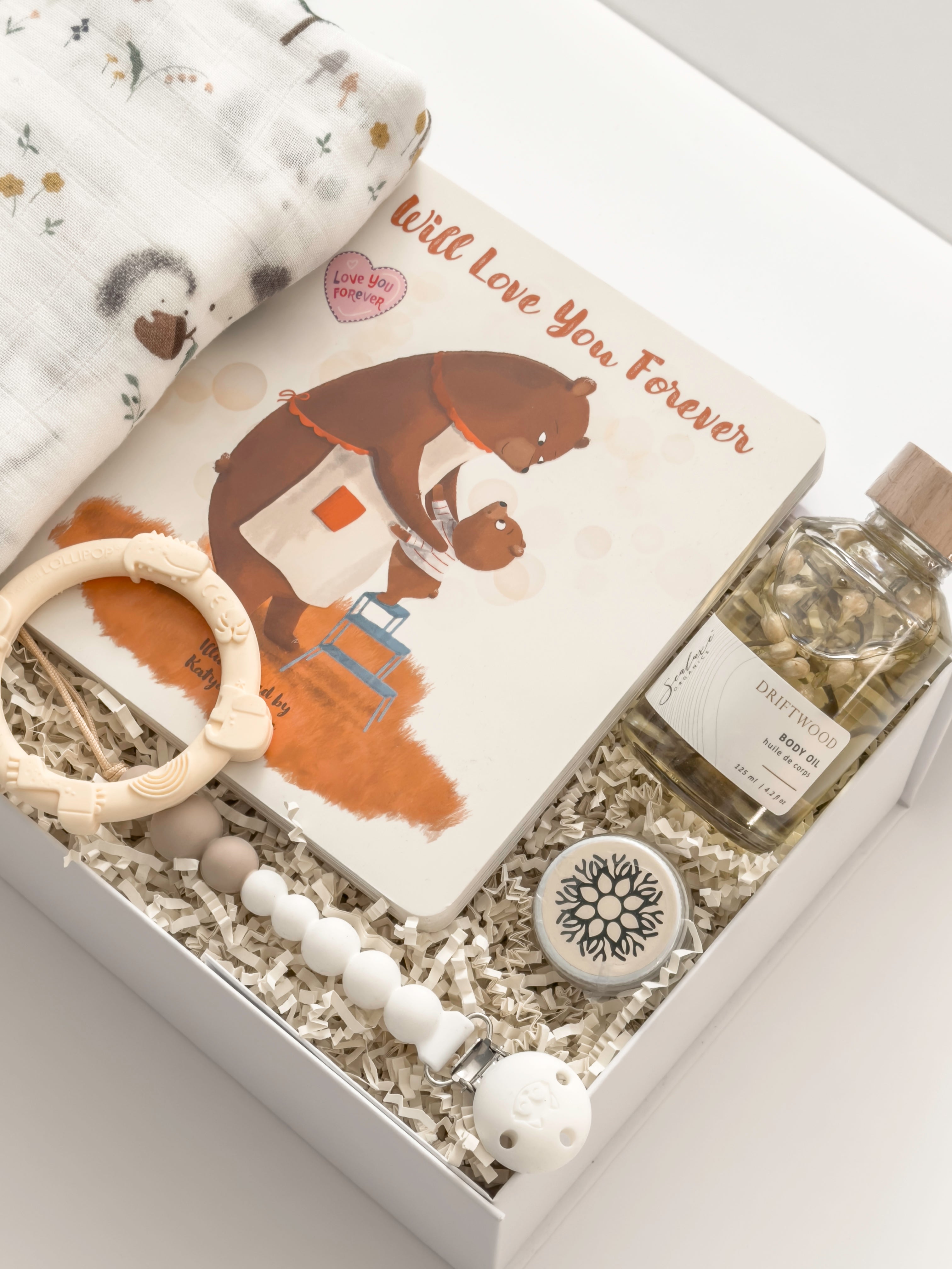Gender-neutral baby gift for new parents by Muse Baskets and Co., presented in a signature white gift box with a swaddle, keepsake book and newborn essentials.