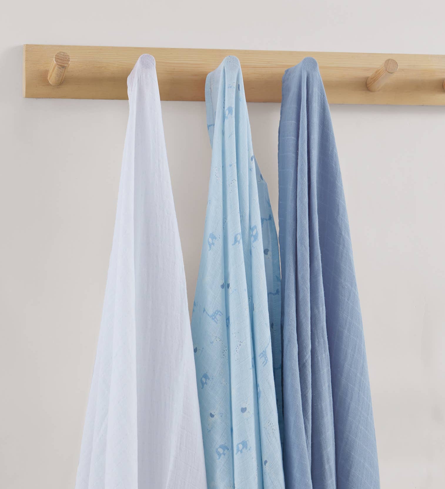 Three baby blankets in white, blue, and gray hanging on a wooden rack against a light background.
