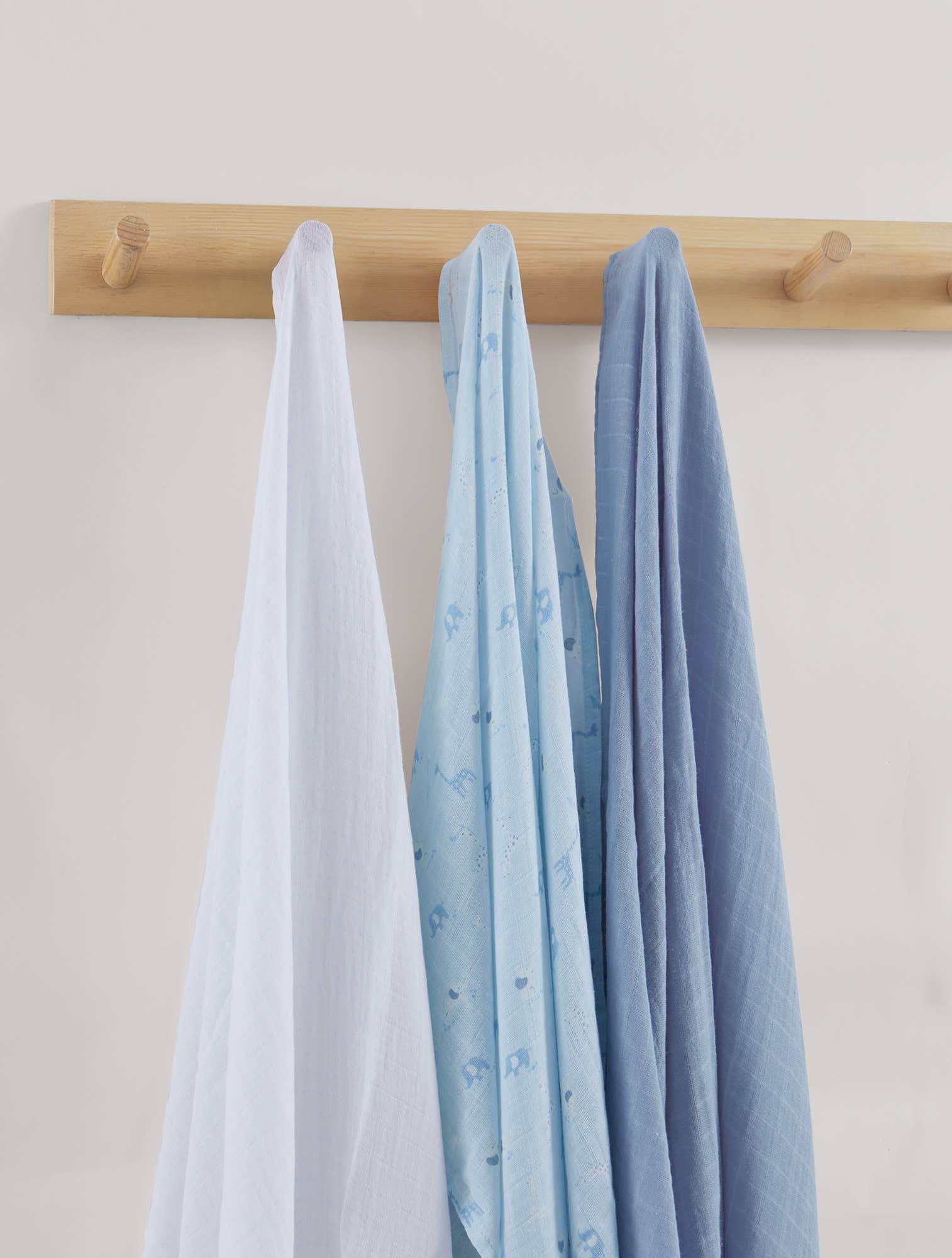 Three baby blankets in white, blue, and gray hanging on a wooden rack against a light background.