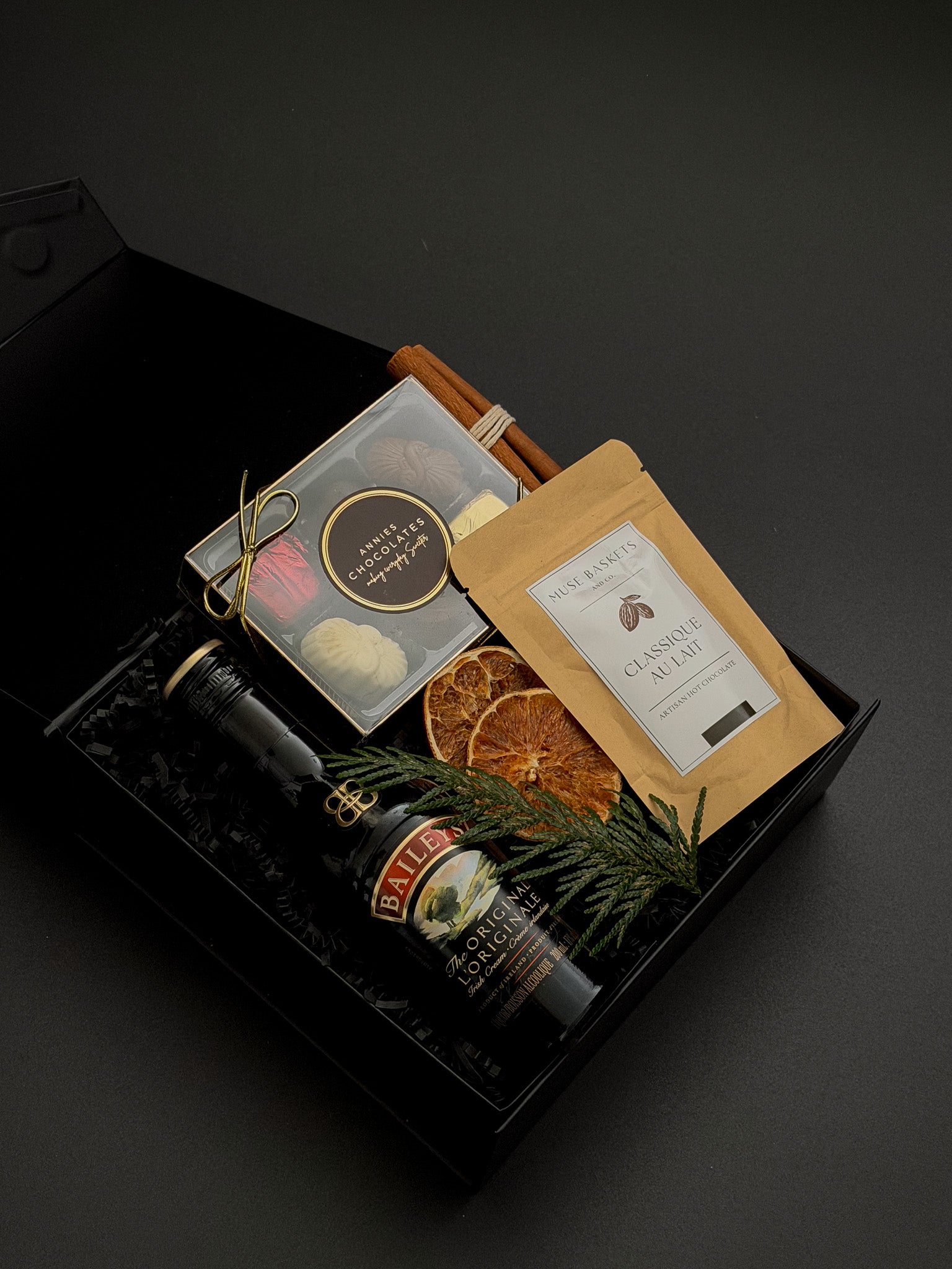 Corporate holiday gift box by Muse Baskets and Co. with Baileys, chocolate, hot chocolate, evergreen accents and satin ribbon for client appreciation.