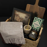 Realtor possession day gift featuring framed vintage-style artwork, wood serving board, striped kitchen towel, candle and pantry accents in a woven keepsake basket.