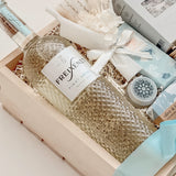 Seraphine bridal gift box by Muse Baskets and Co. shown from above, with Freixenet Pinot Grigio, Sealuxe Ocean Goddess bath tea, a Muse candle, olive and bloom handmade soap, artisan chocolate, lip balm, and a white preserved floral bouquet in a wood crate tied with baby blue ribbon, a refined wedding, engagement, and bridal shower gift from Canadian makers.