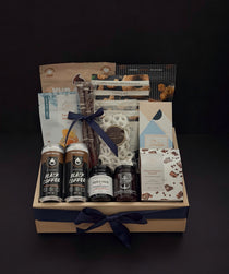 Canadian Gourmet gift box by Muse Baskets and Co., front view of a natural wood crate of Canadian-made chocolate, coffee, cookies, cashews, and preserves finished with a navy satin ribbon, styled as a realtor closing, homeowner welcome, and corporate gift.
