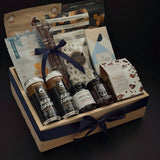 Canadian Gourmet gift box by Muse Baskets and Co. shown at an angle, a wood crate holding Two Bears flash brew coffee, Chez Christophe chocolate, Saltspring Kitchen Co. pepper spread, and white chocolate pretzels tied with a navy satin ribbon for realtor closing and corporate gifting.