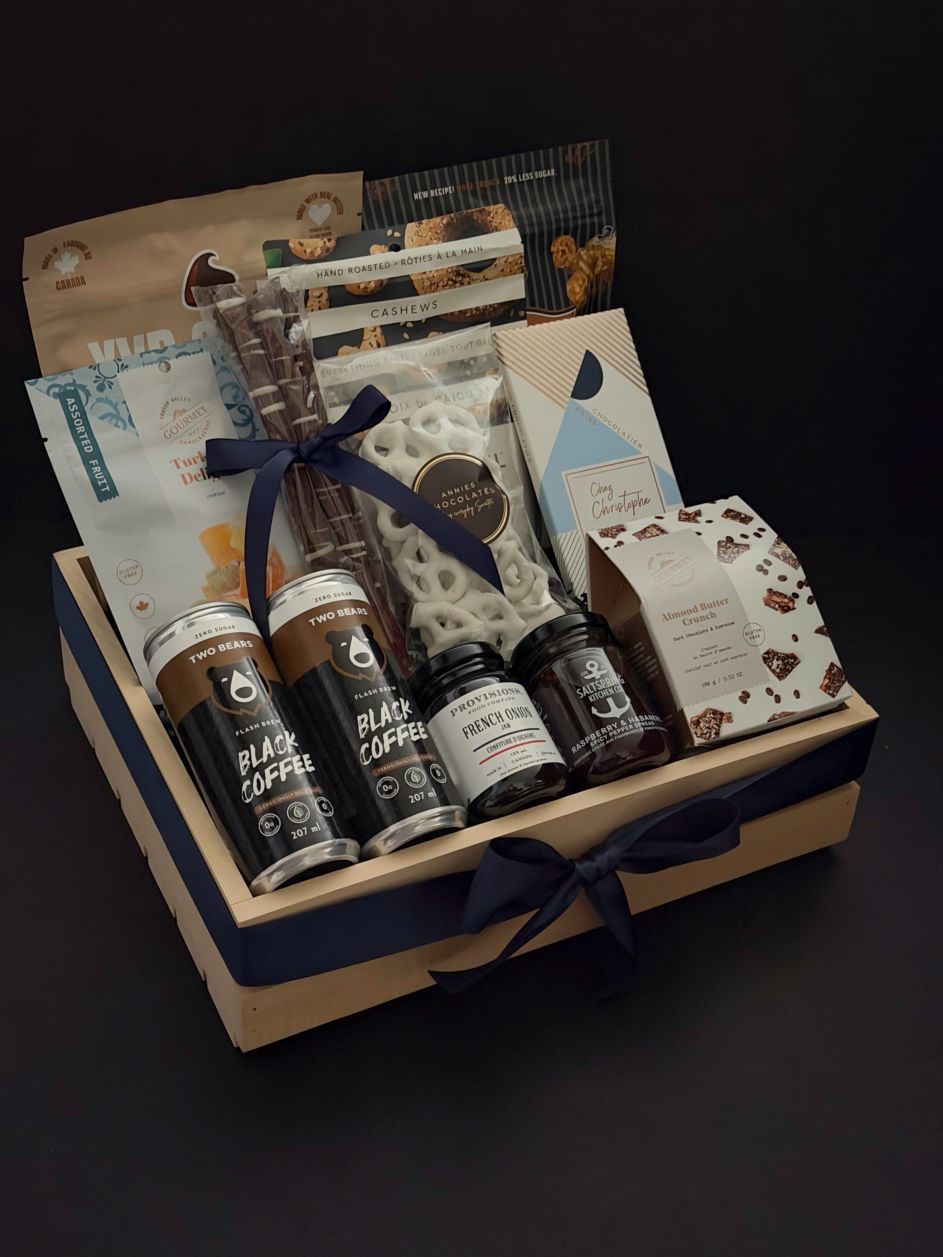 Canadian Gourmet gift box by Muse Baskets and Co. shown at an angle, a wood crate holding Two Bears flash brew coffee, Chez Christophe chocolate, Saltspring Kitchen Co. pepper spread, and white chocolate pretzels tied with a navy satin ribbon for realtor closing and corporate gifting.