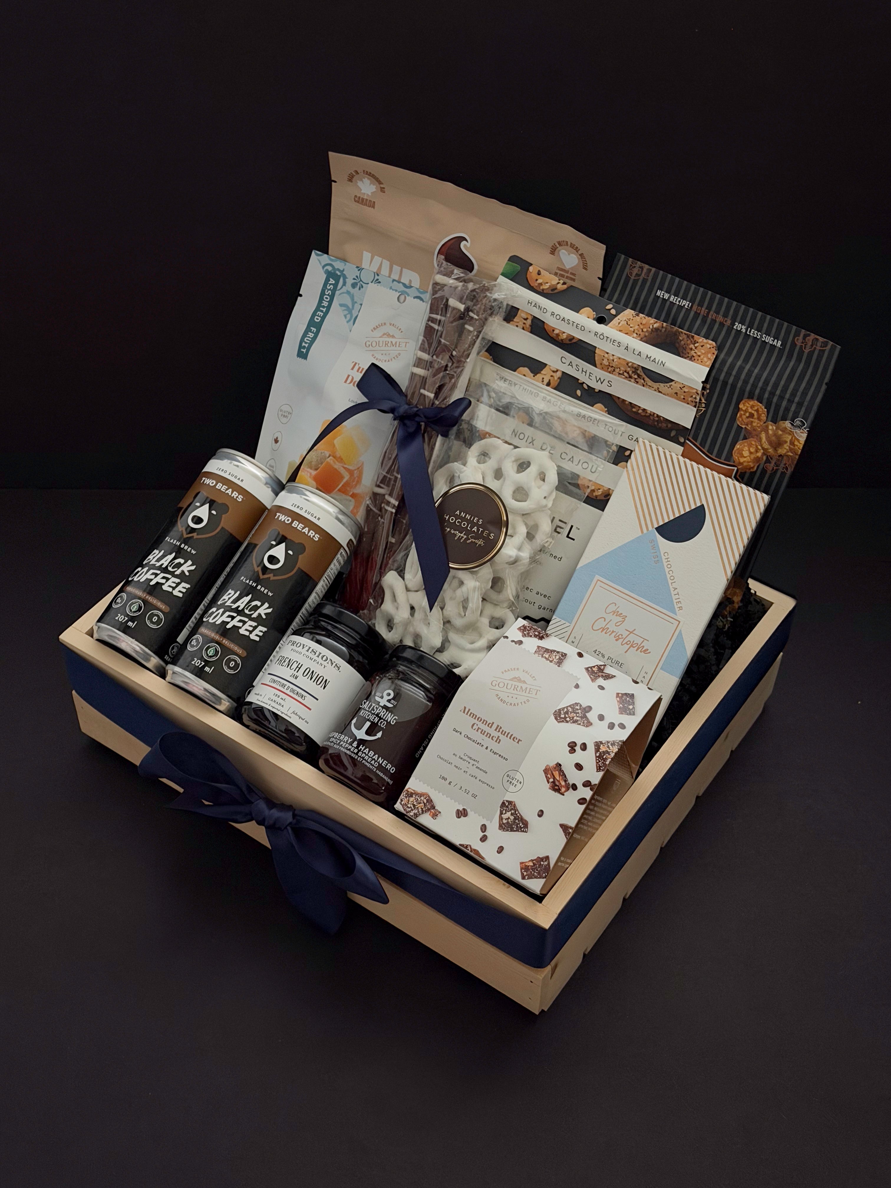 Canadian Gourmet artisan gift box by Muse Baskets and Co., an angled view of a wood crate filled with Canadian small-batch makers including coffee, chocolate bark, French onion jam, and everything bagel cashews, finished with a navy satin ribbon as a homeowner welcome and client appreciation gift.