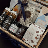 Canadian Gourmet gift box by Muse Baskets and Co., close-up of Two Bears flash brew coffee, Provisions French onion jam, Saltspring Kitchen Co. raspberry habanero spread, Fraser Valley Gourmet almond butter crunch, and white chocolate pretzels in a navy-ribboned wood crate, a luxury Canadian gift for closings and corporate occasions.