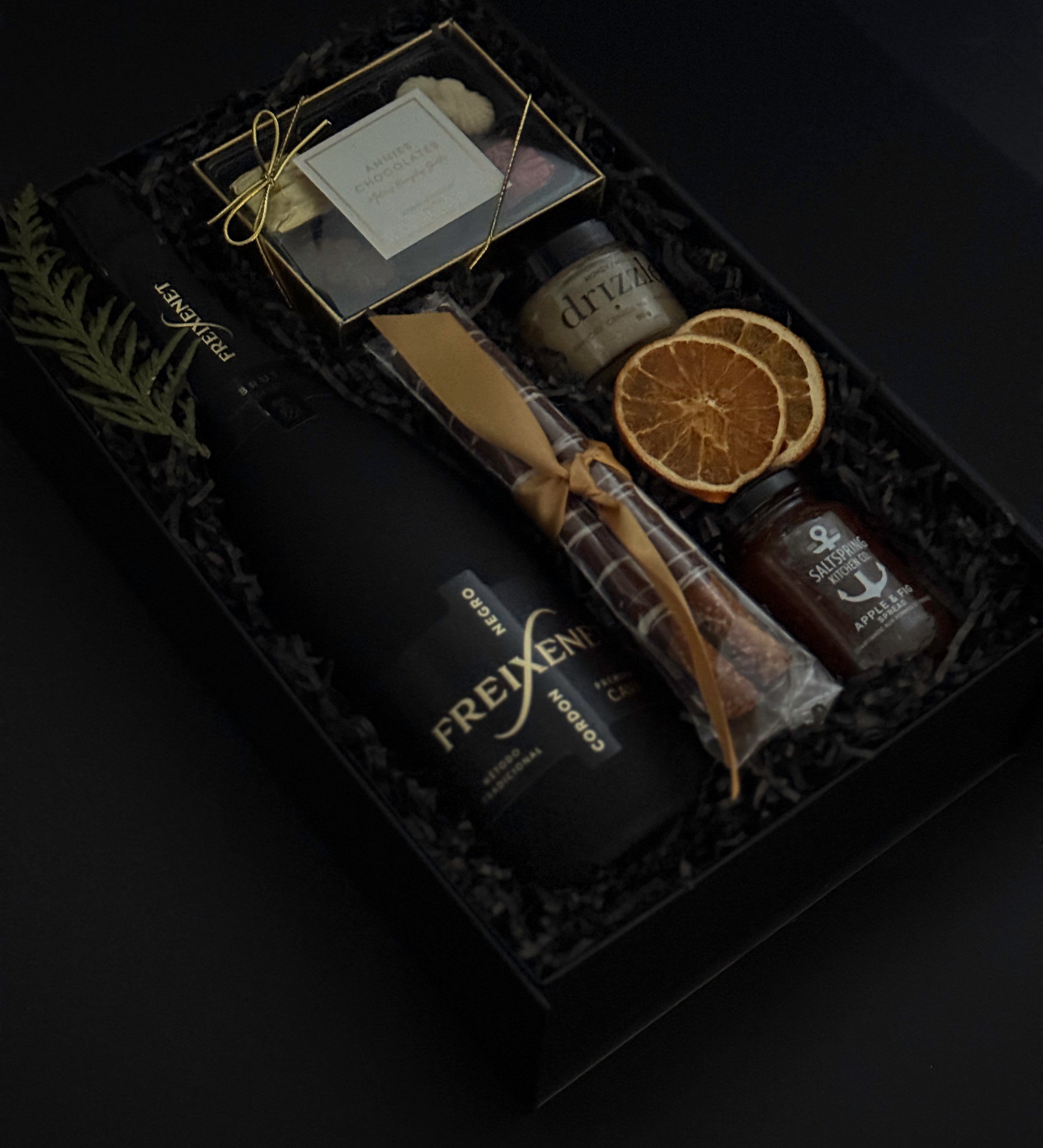 Obsidian Celebration Box with sparkling wine, chocolates, pretzels, honey, and fig spread arranged in a black gift box with festive greenery and ribbon.