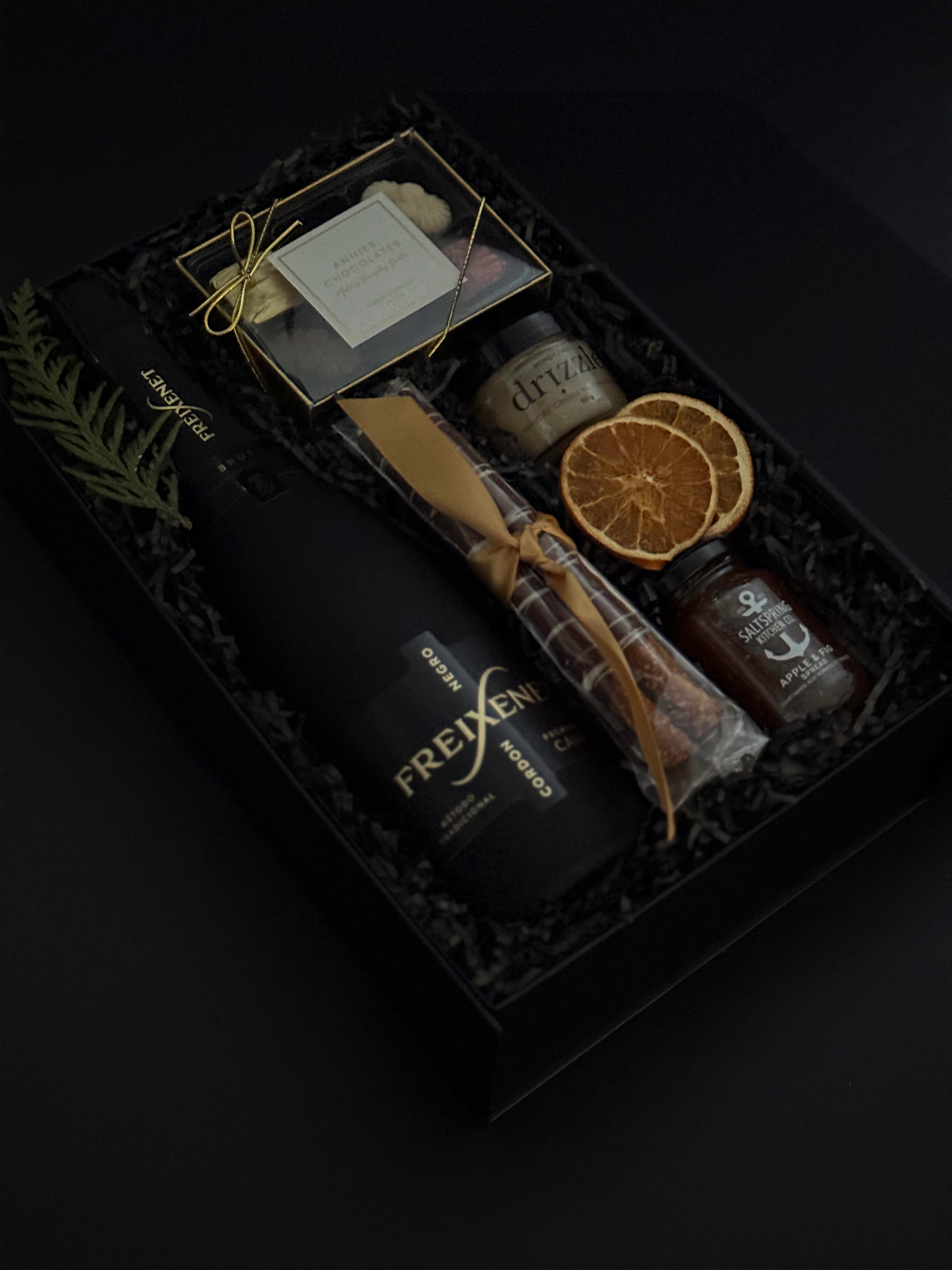 Obsidian Celebration Box with sparkling wine, chocolates, pretzels, honey, and fig spread arranged in a black gift box with festive greenery and ribbon.