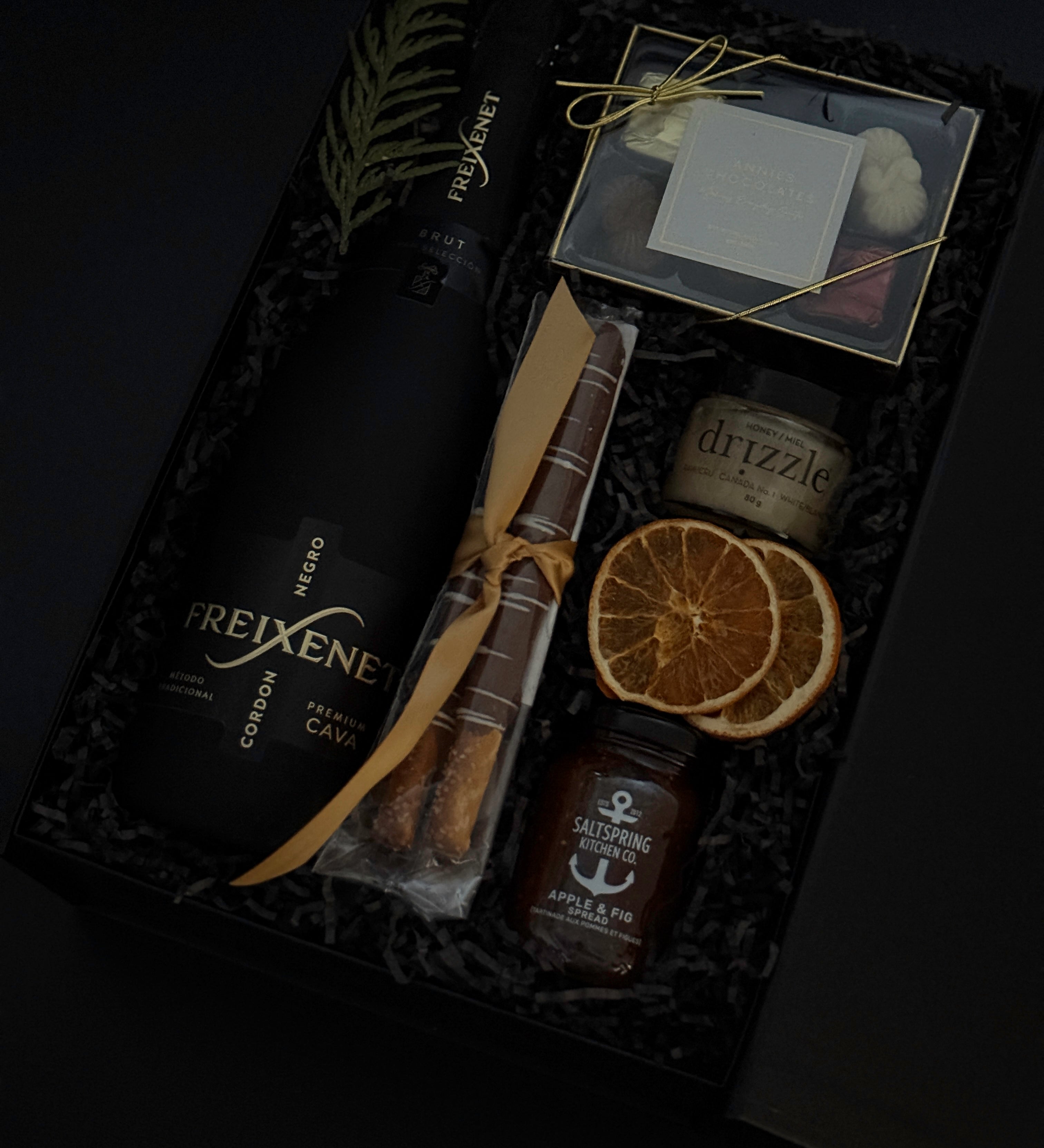 Obsidian Celebration Box with sparkling wine, chocolates, pretzels, honey, and fig spread arranged in a black gift box with festive greenery and ribbon.